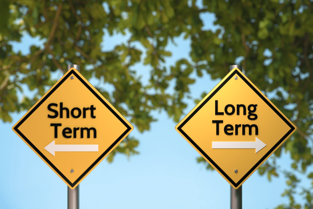 two yellow signs in front of tree branches. one says short term and the other says long term.