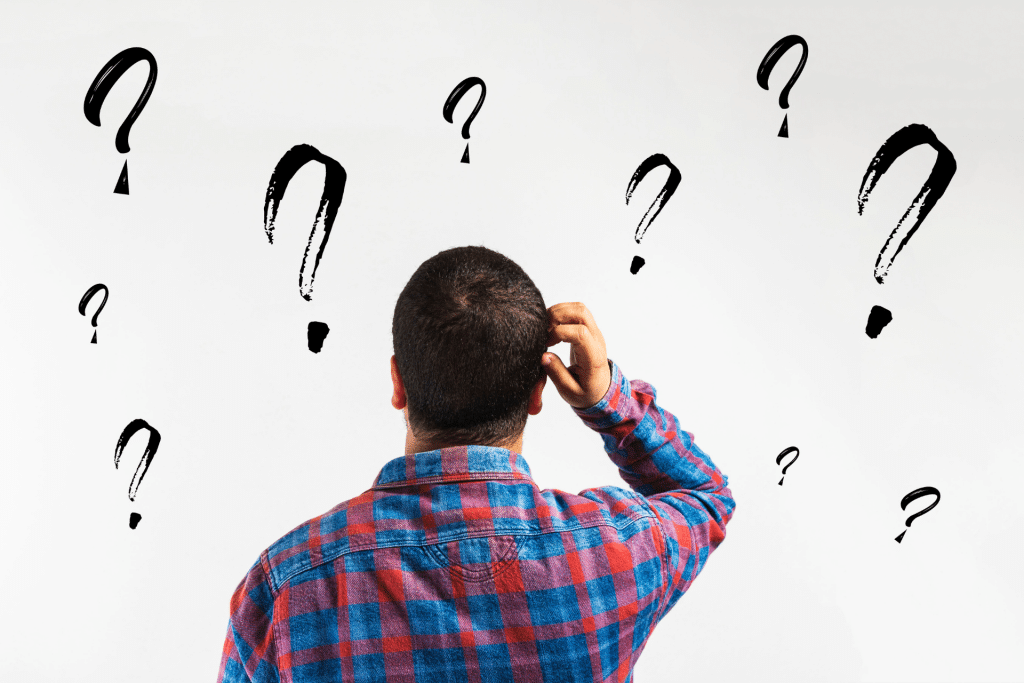 man scratching his head looking at a wall with black question marks on it