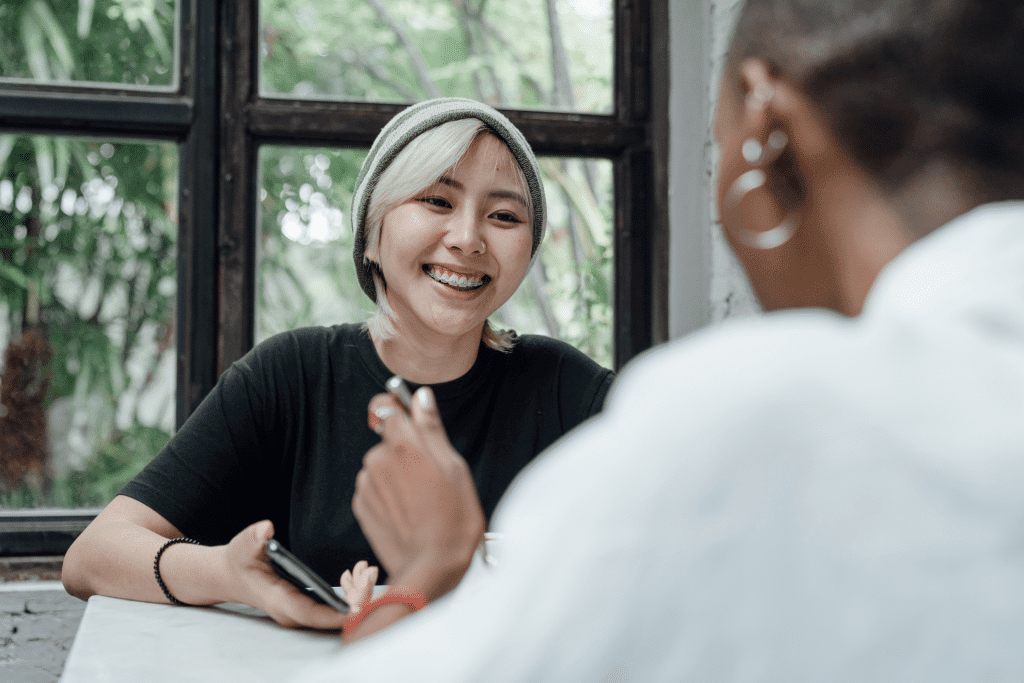 Two women talking to each other. One woman's face is in view and is smiling.