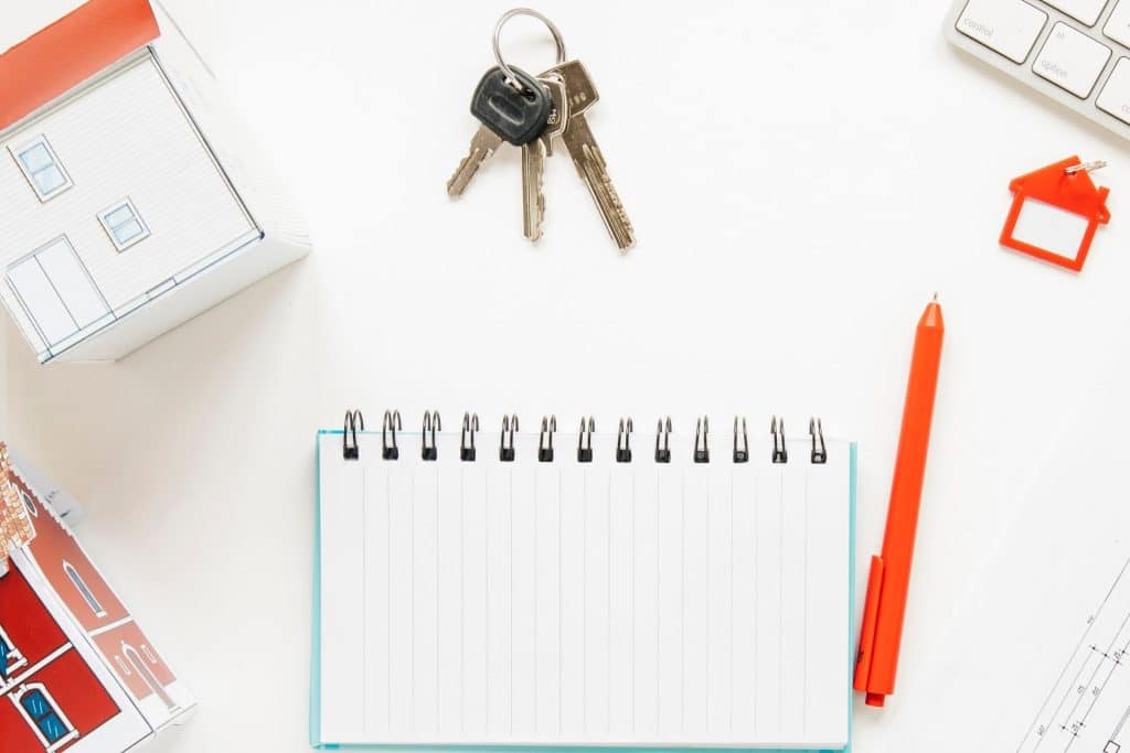 A high angle view of of two house models, positioned alongside a spiral notepad, keys, and a pen on a white table. This imagery signifies a focus on SFR real estate investing.