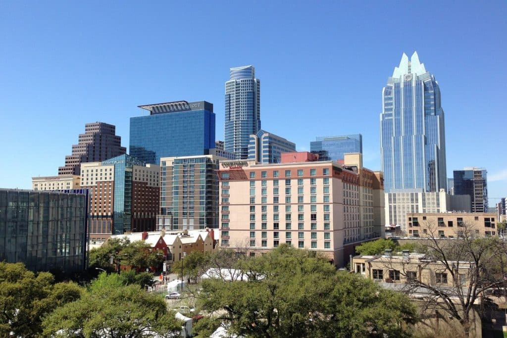 The view of Austin's vibrant city filled with towering buildings against a clear blue sky and trees below to symbolize Austin real estate investing.