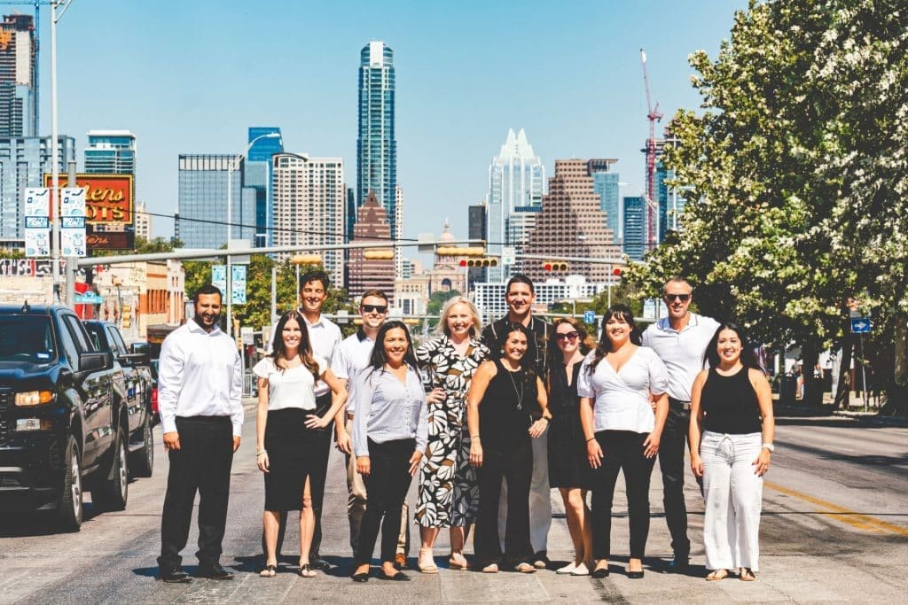 The 1836 Property Management team standing in the middle of a road, with building of Austin City in the background.