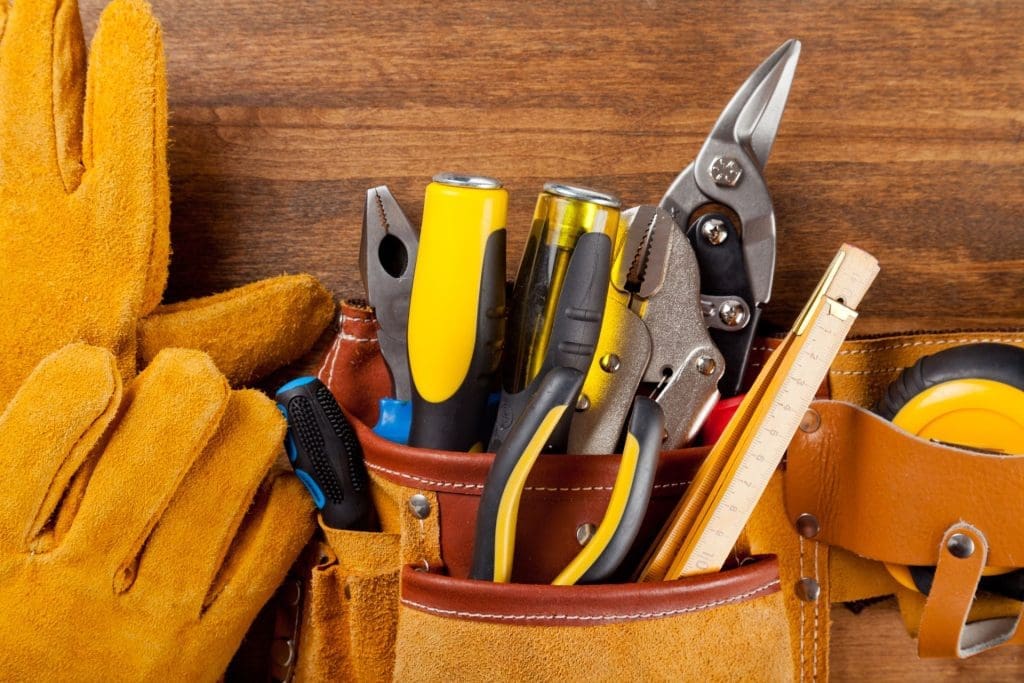 Tools in a leather tool belt on a wooden surface, representing essential equipment for Austin property management.